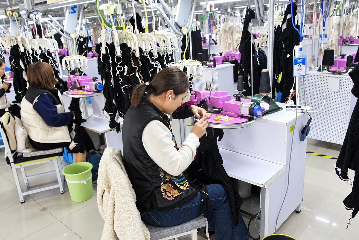 Worker joining knitted garment panels at a linking machine.