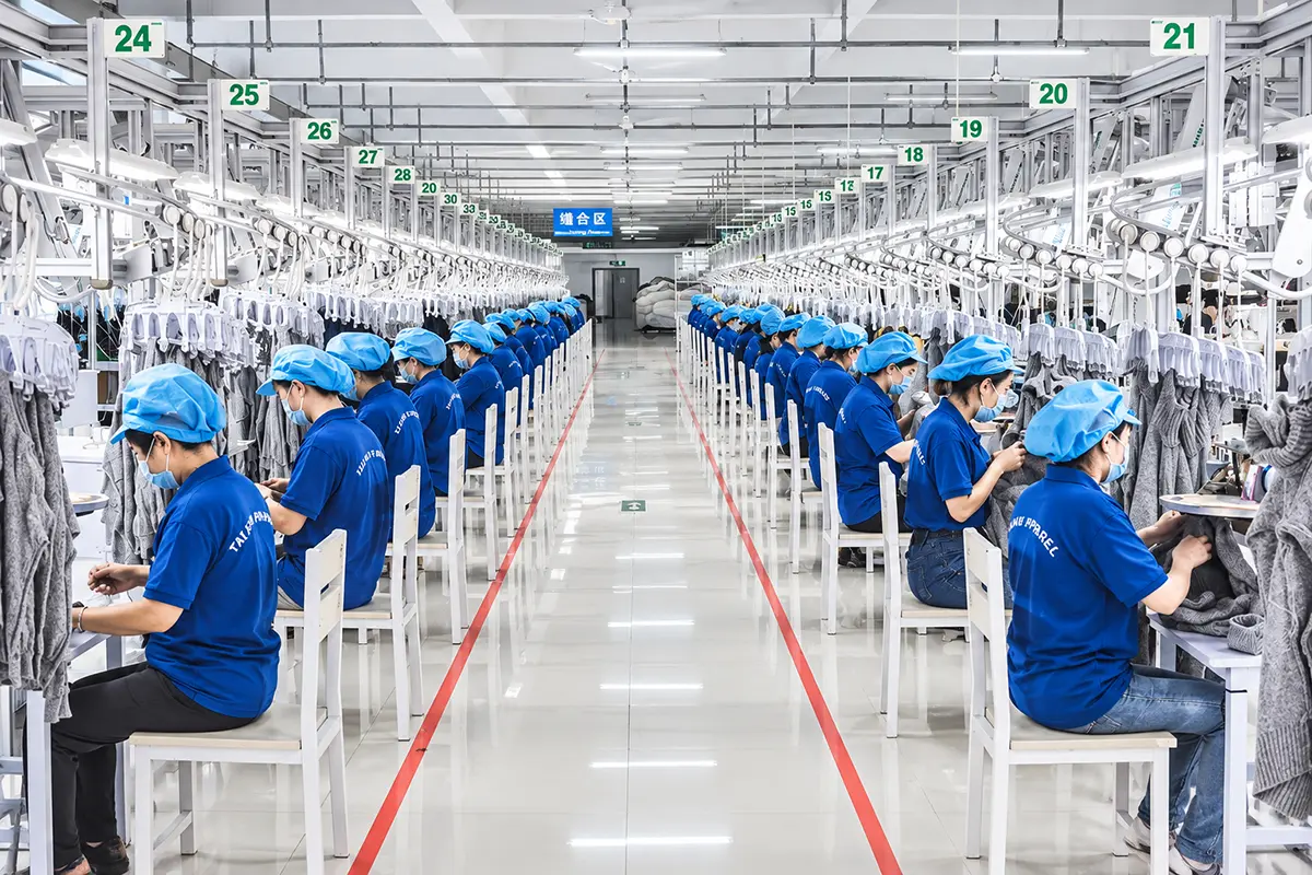 Factory team members working on knitted garments at rows of production stations.