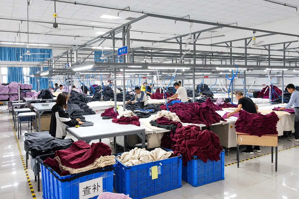 Workers handling knitwear at tables in a garment finishing workshop.