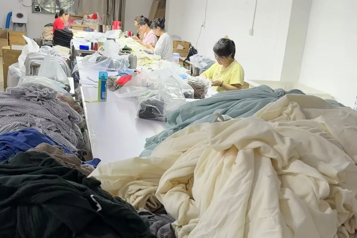 Workers handling knitwear at a long factory work table.