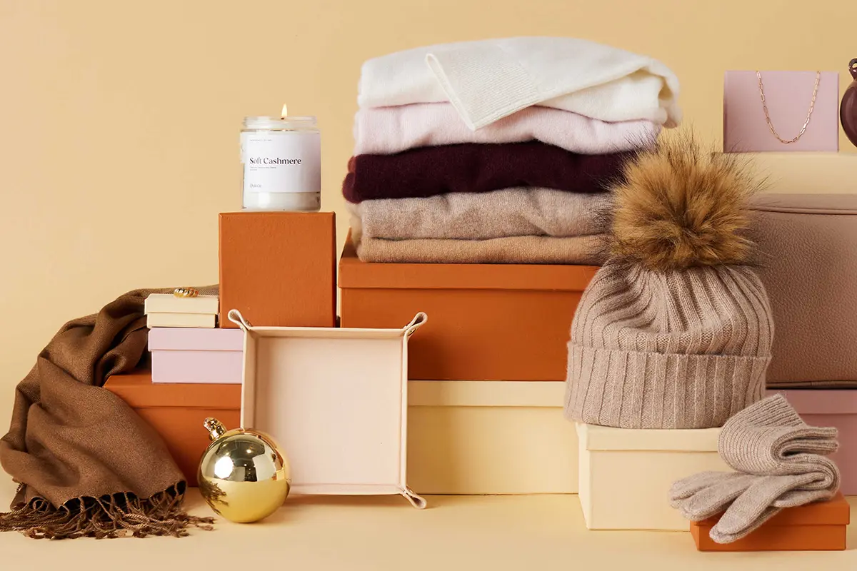 Folded sweaters, a knit hat, gloves, and a scarf displayed with gift boxes.