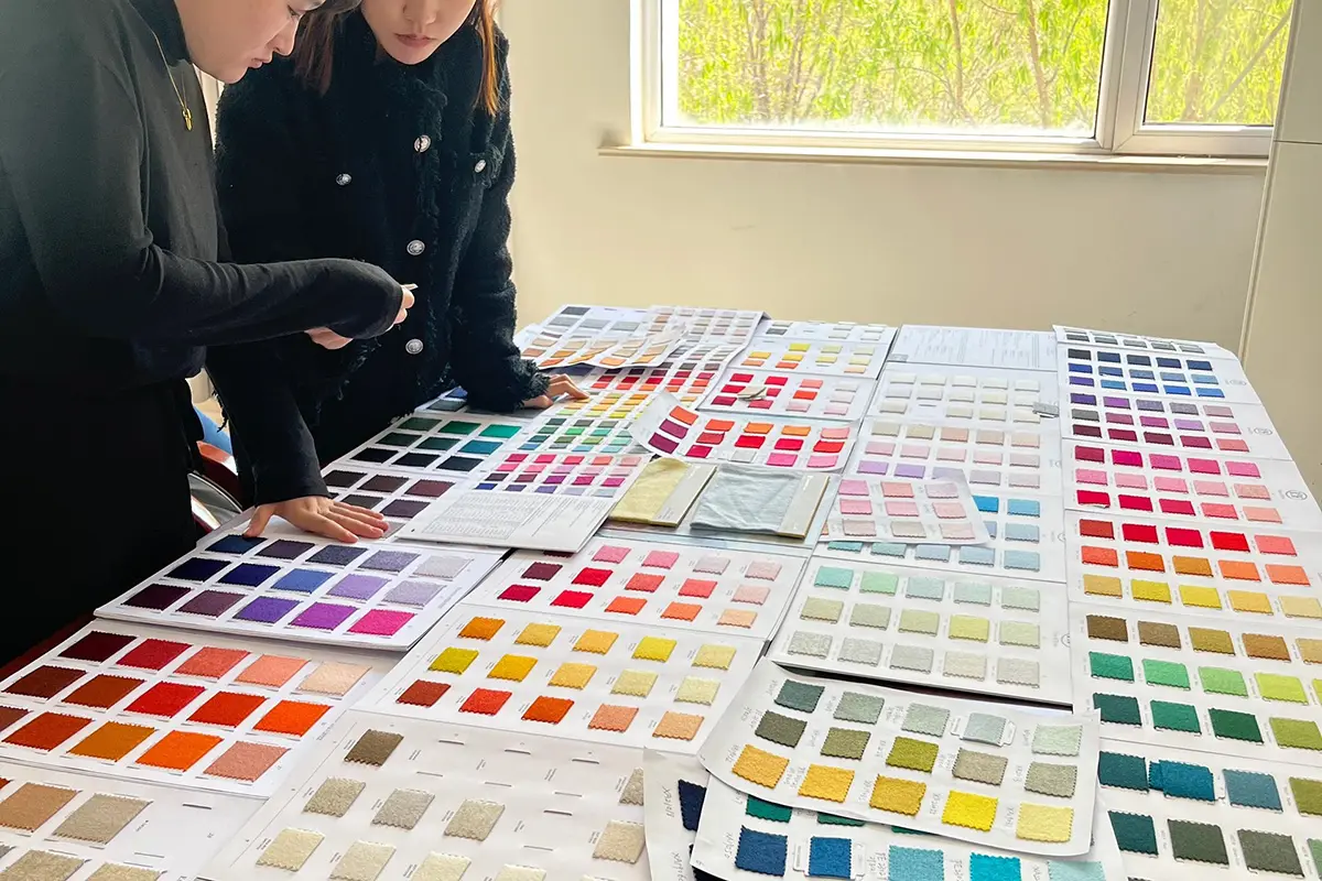Two people reviewing knitted color swatches spread across a table.
