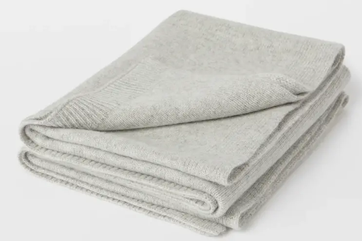 Folded light gray knitted blanket with ribbed edging.