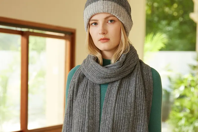 Woman wearing a gray ribbed scarf and a two-tone knit beanie.