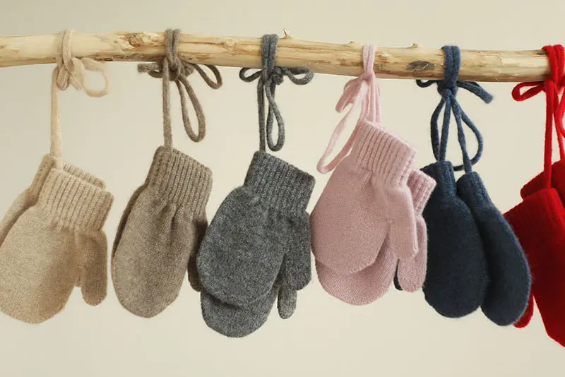 Knitted mittens in assorted colors hanging by ties from a wooden branch.