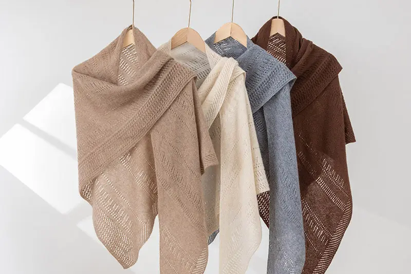 Open-knit shawls in taupe, cream, blue-gray, and brown on wooden hangers.