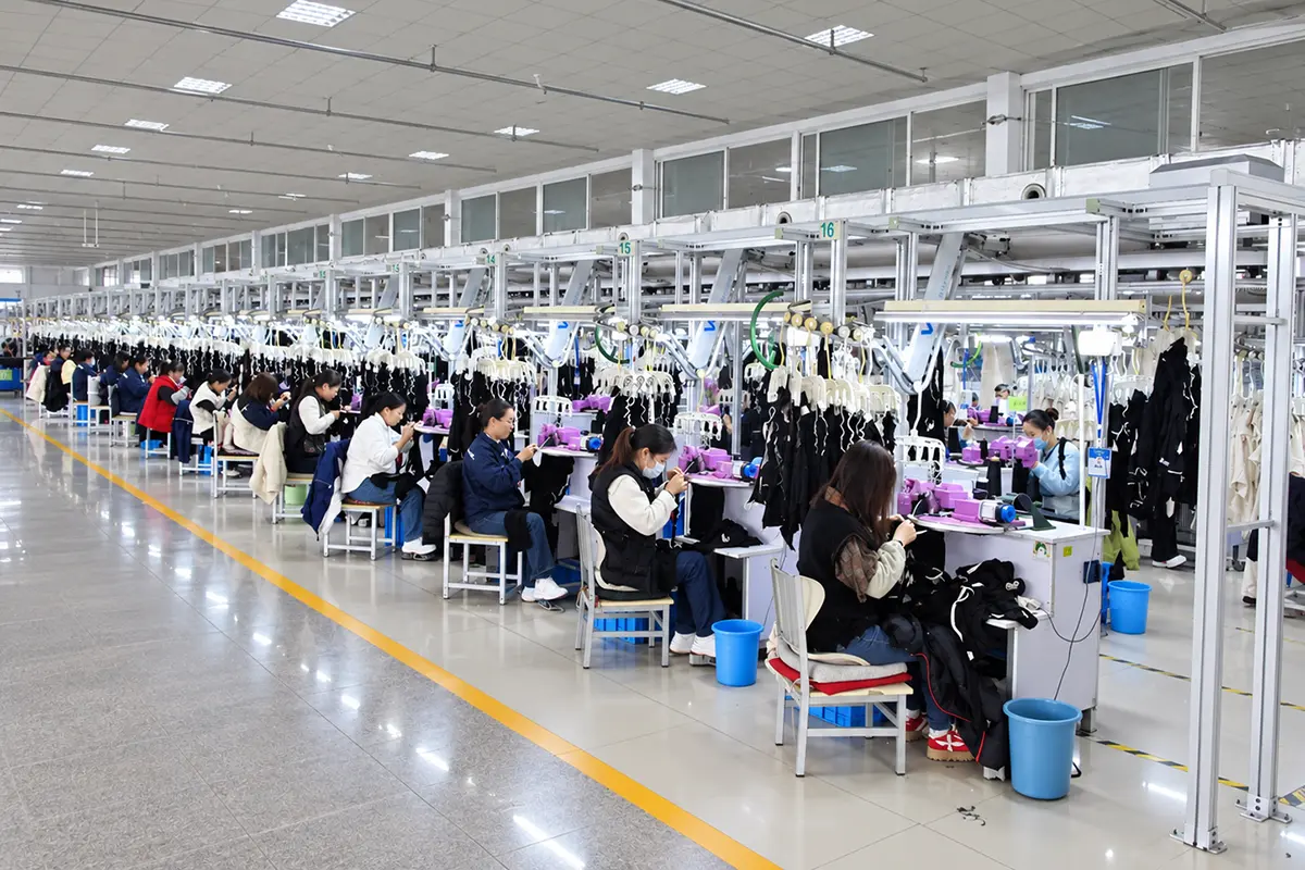 Workers handling knit garments at workstations in a production workshop.