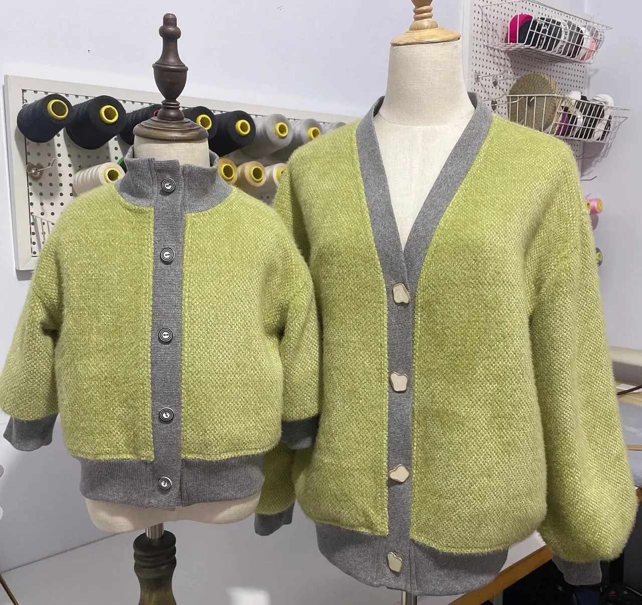 Two green cardigan samples with gray trim on dress forms.
